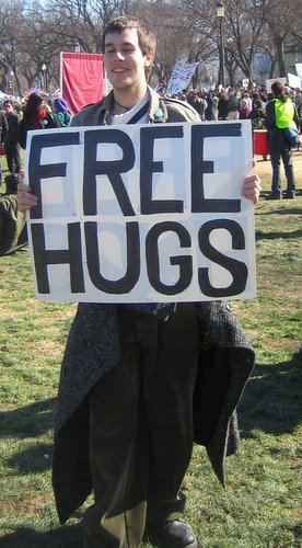 man holding a free hugs sign in the park