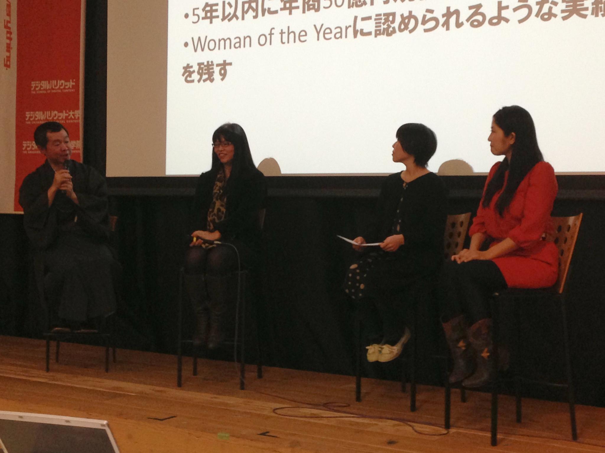 people sitting on stage while a screen displays a woman at a conference