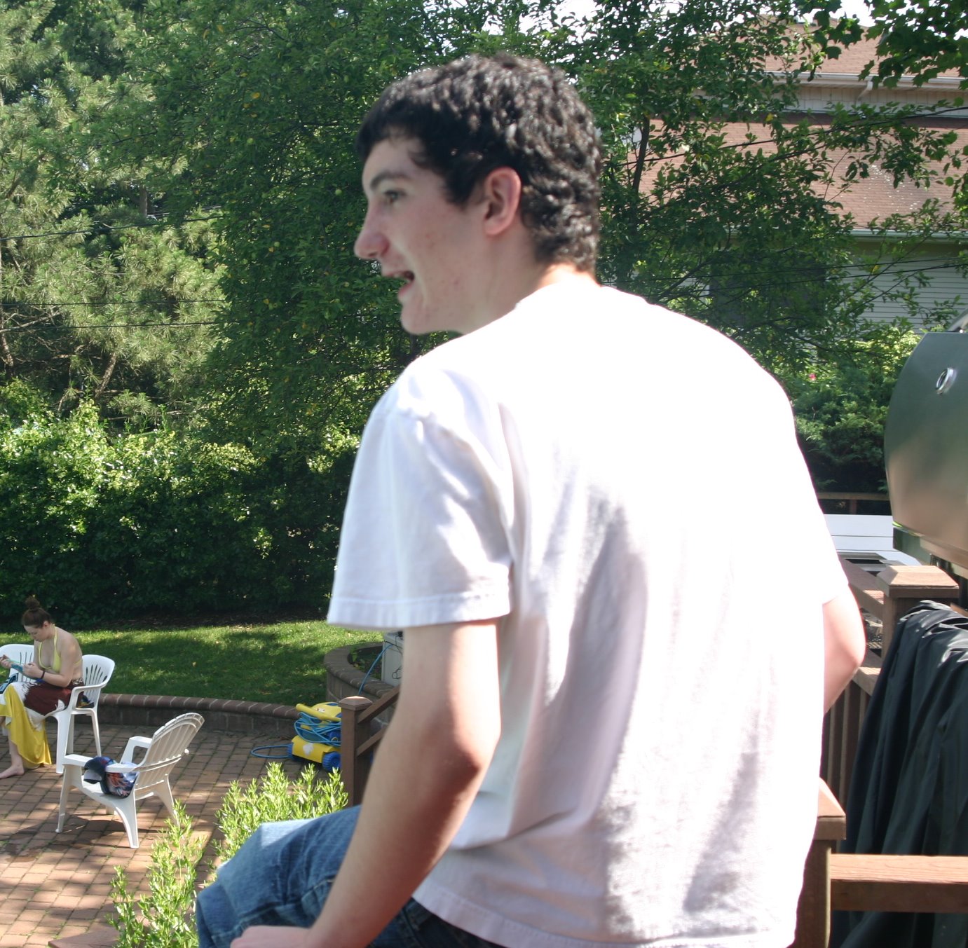 a young man in a white shirt standing in front of some people on the patio
