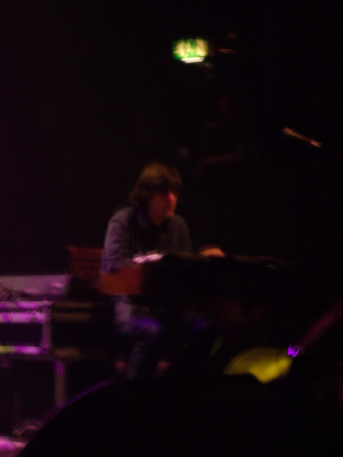 a man in dark concert, and a band on stage behind him