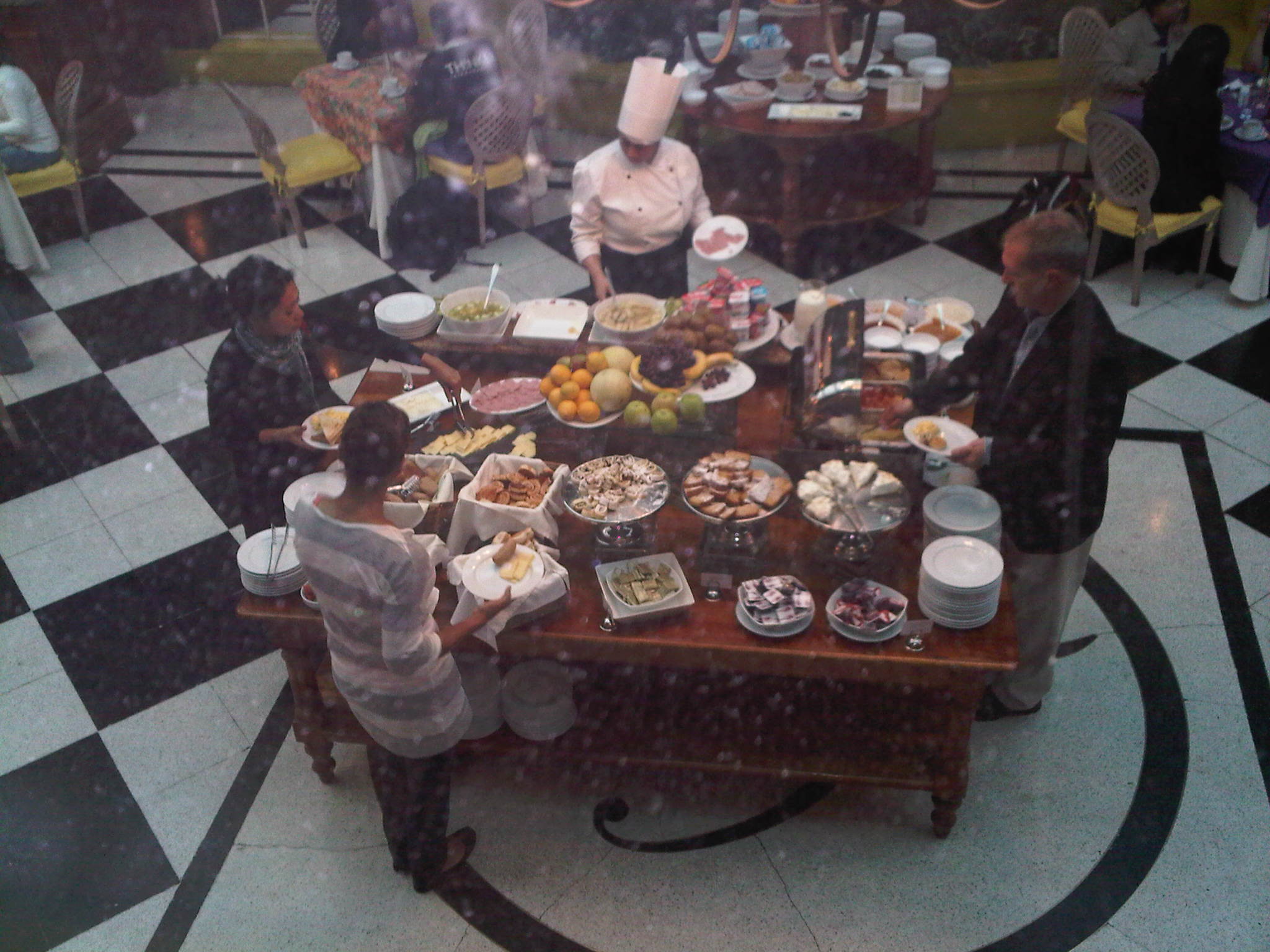 an array of people standing around a dining table full of food