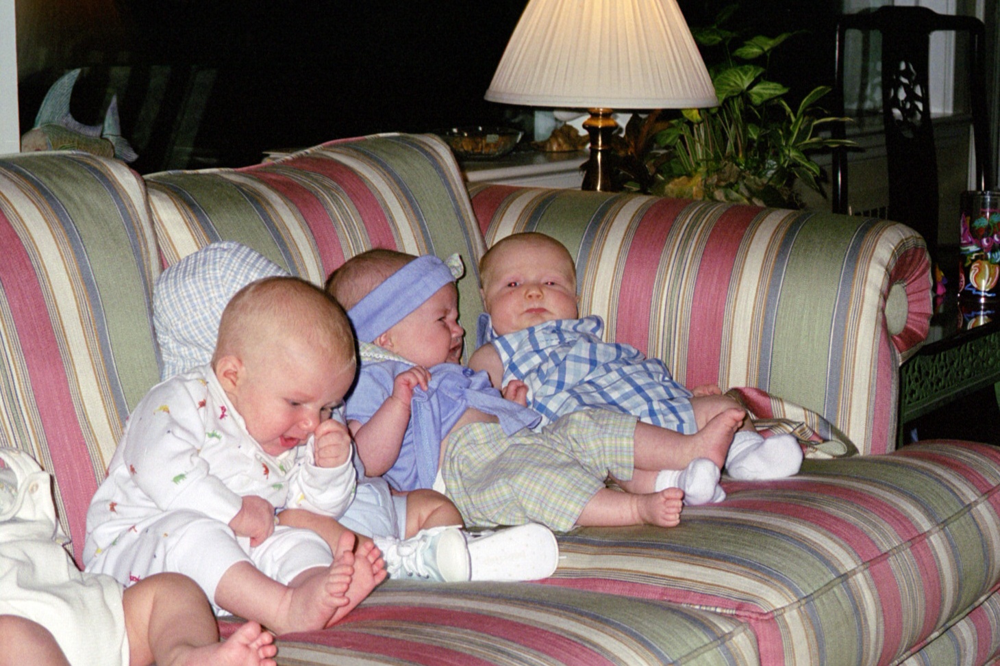 three babies in pajamas sitting on a striped sofa
