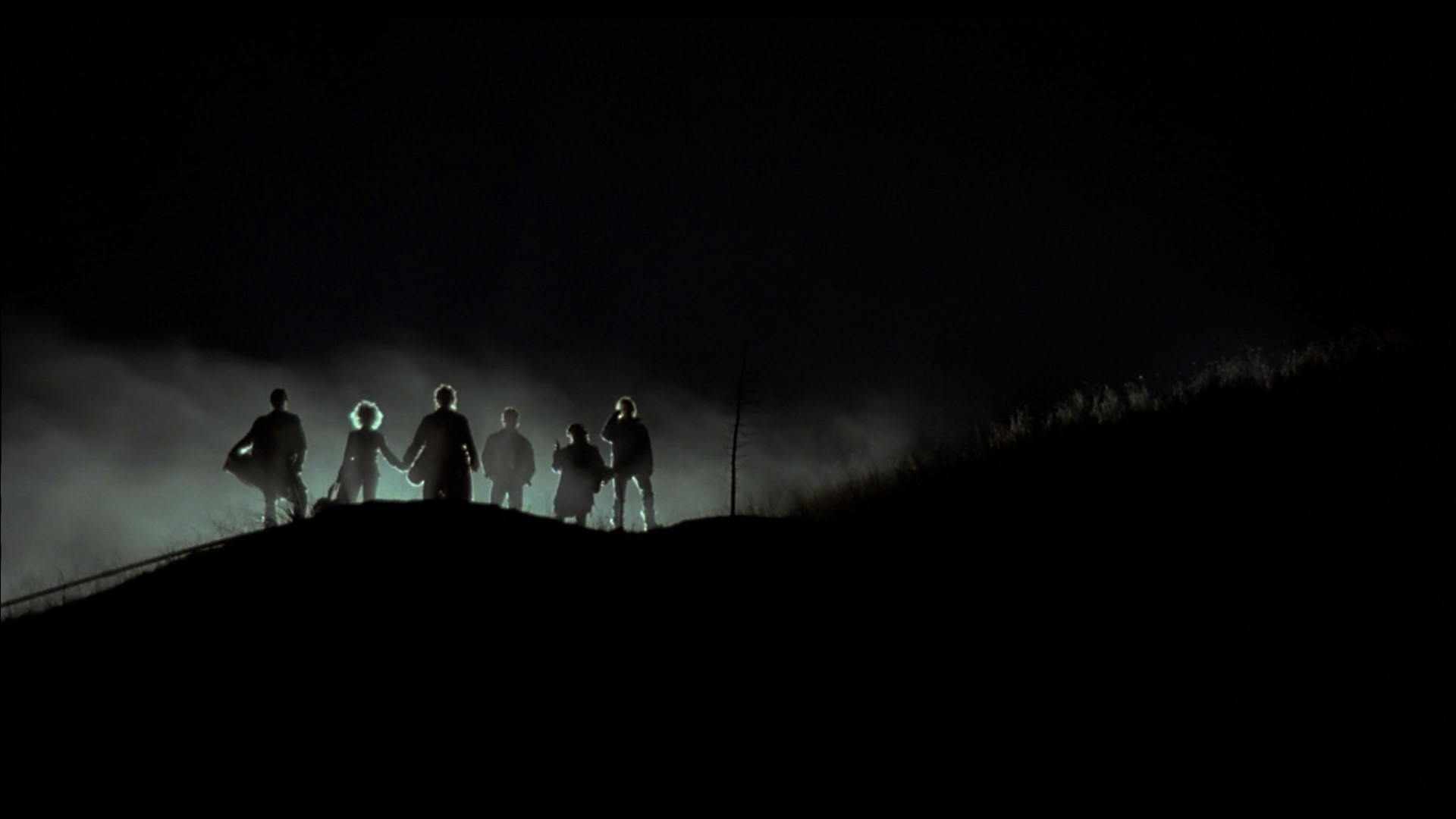 a group of silhouetted people walk up a steep hill