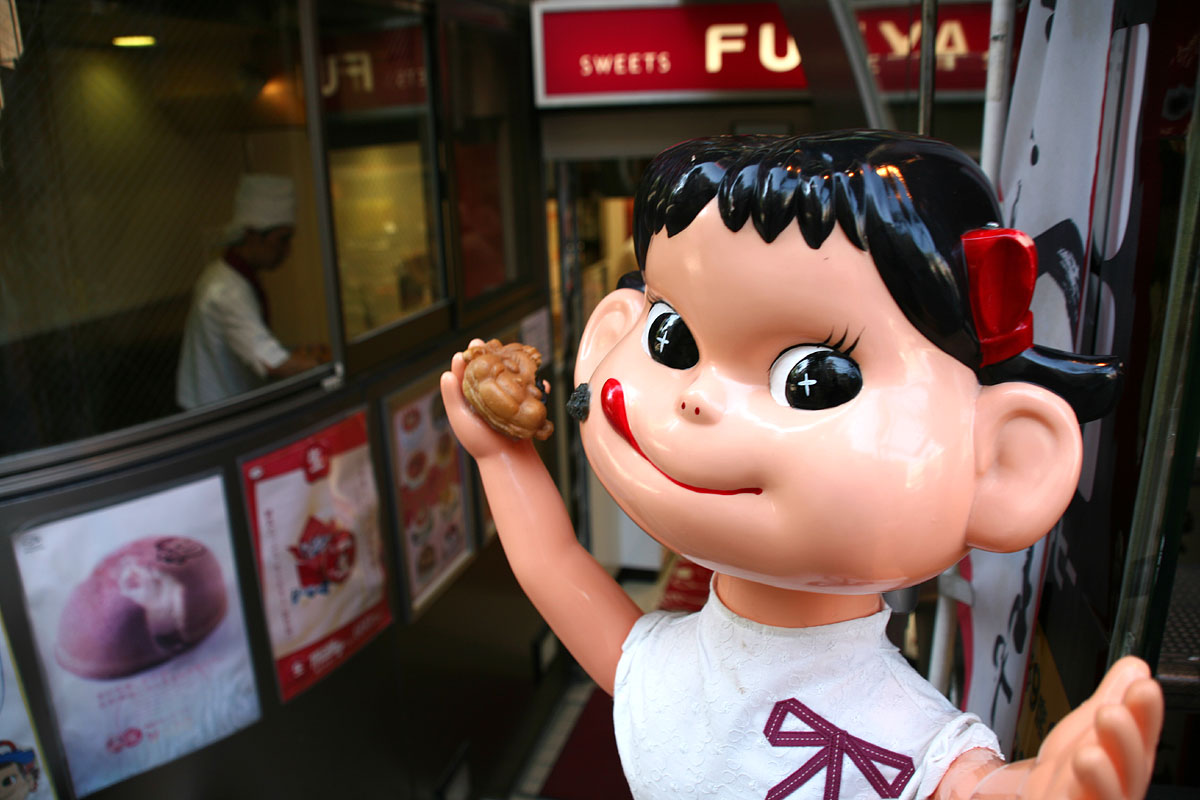 a fake child is holding up a donut and standing in front of the shop