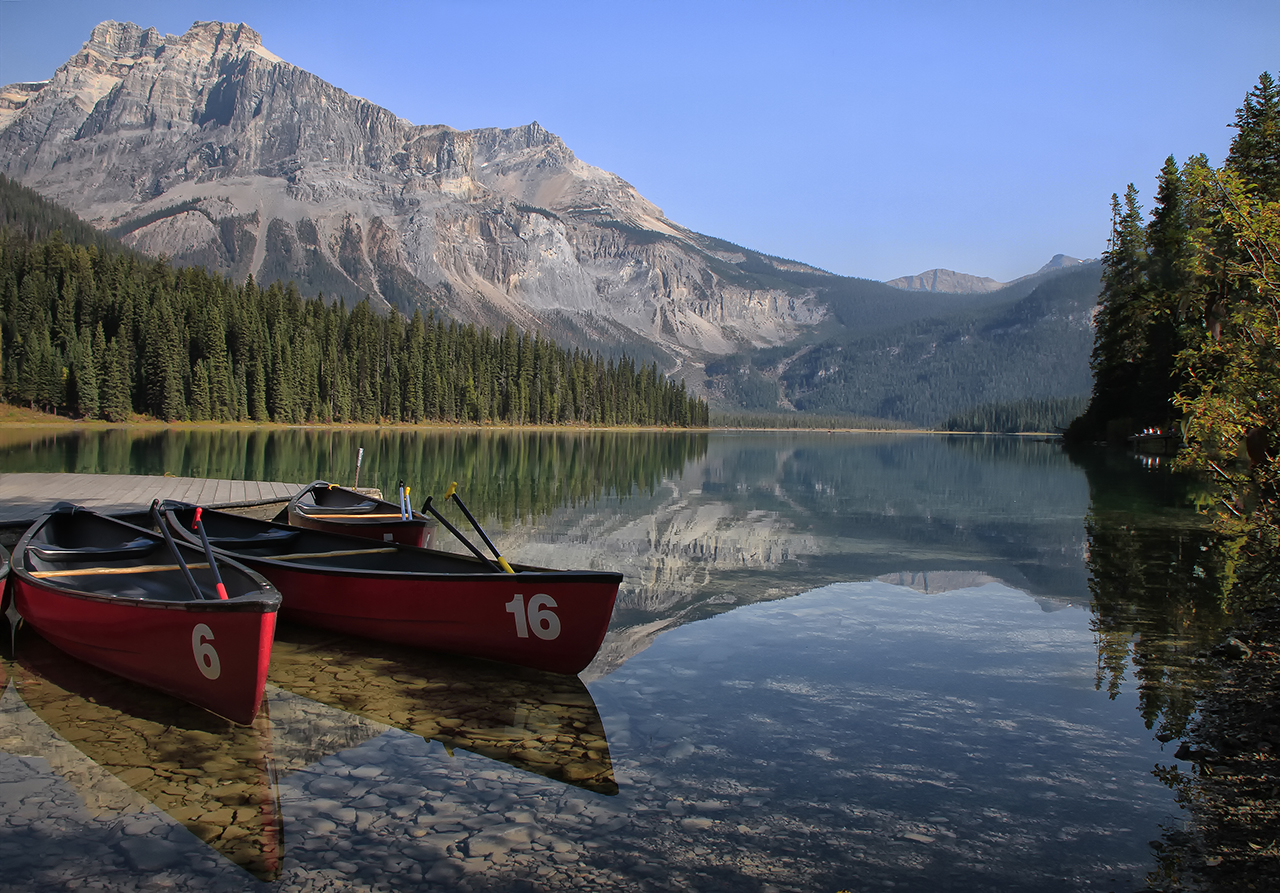 boats are parked at the shore of a calm mountain lake