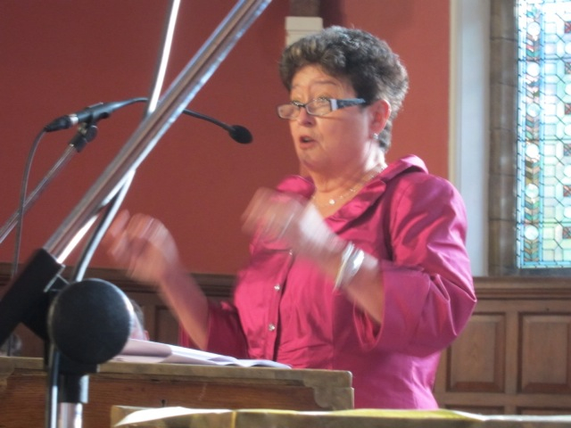 a woman holding a mic speaking from behind a microphone