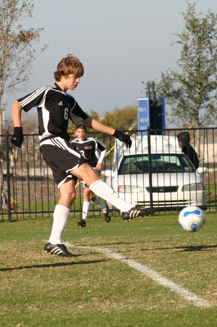 young male soccer player kicking ball in grassy field