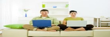 man and woman sitting on a couch holding laptops
