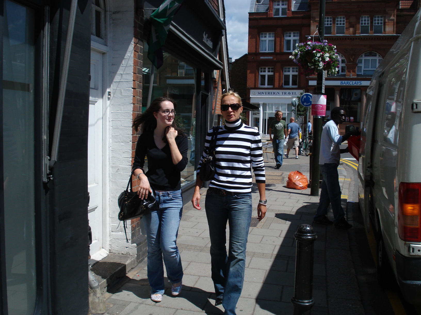 two young women walk down the street on their cell phones