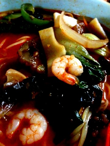 a blue bowl of stew with shrimp, vegetables and other toppings