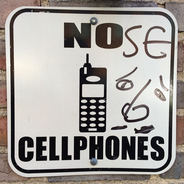 a cellphone warning sign is hung on a brick wall