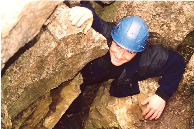 man climbs rocks in black jacket and blue helmet