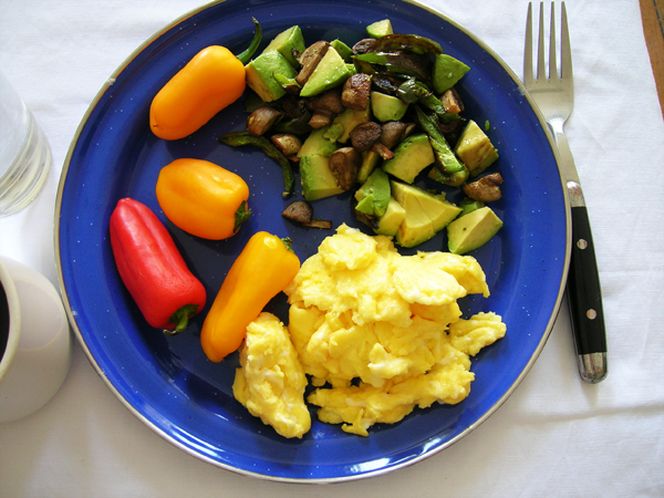 a blue plate with eggs and veggies on a white table