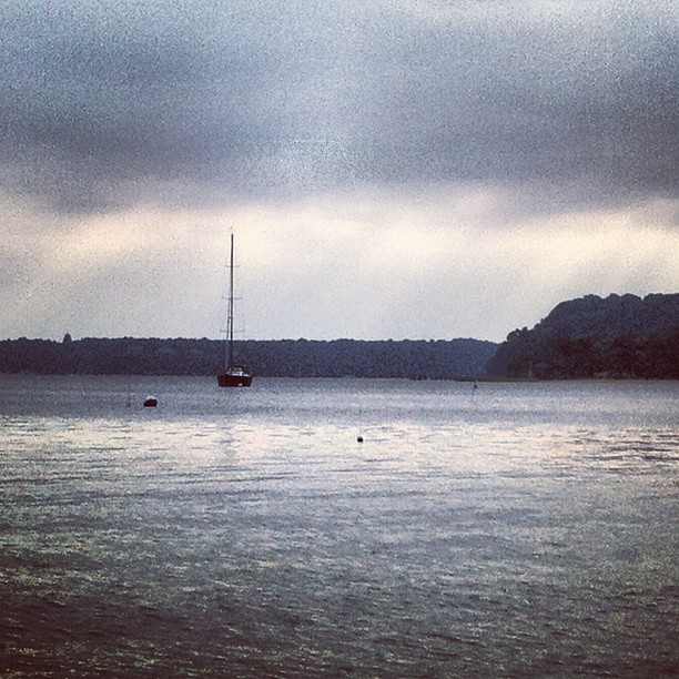 a sailboat floats across a body of water on cloudy day
