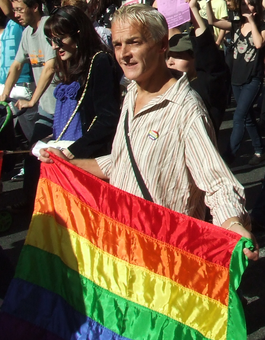 a man carrying a large rainbow flag in a city parade