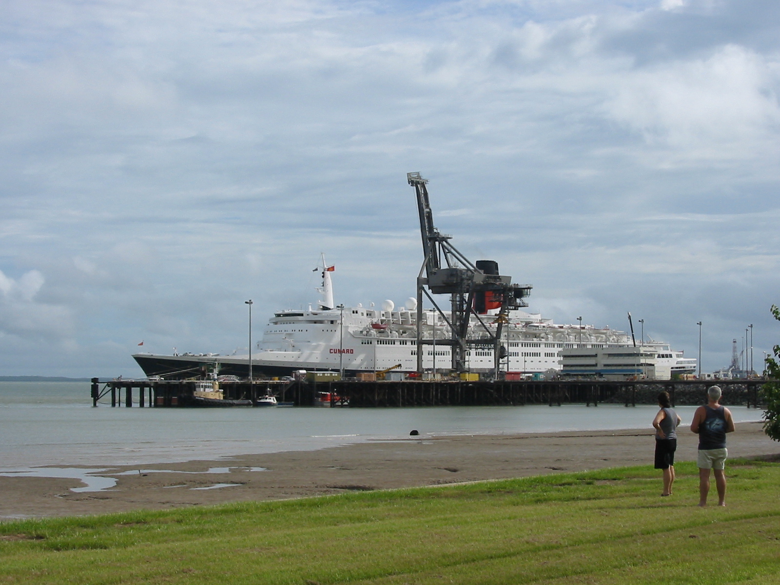 two people walking on grass near water and a ship