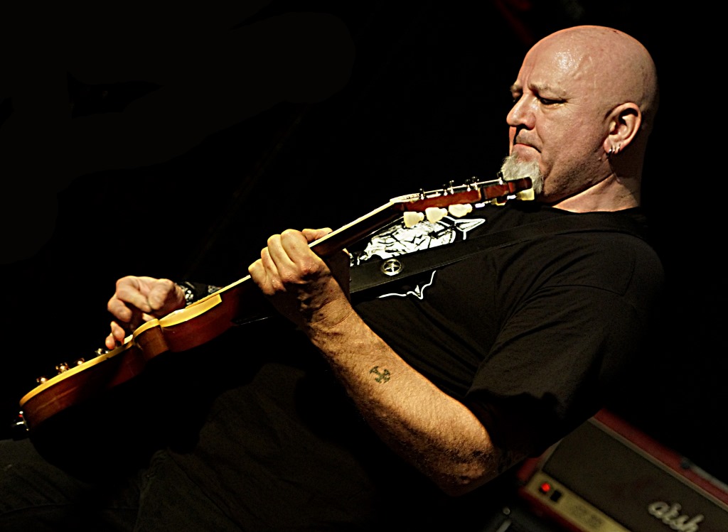 a bald man with a beard playing a guitar