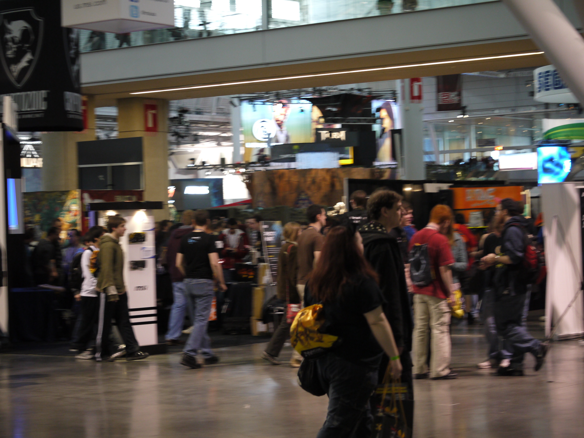 a crowd of people walking through a building next to a television screen