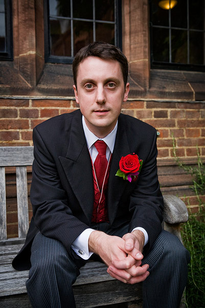 man in black suit sitting on wooden bench with a rose pinned on his lapel