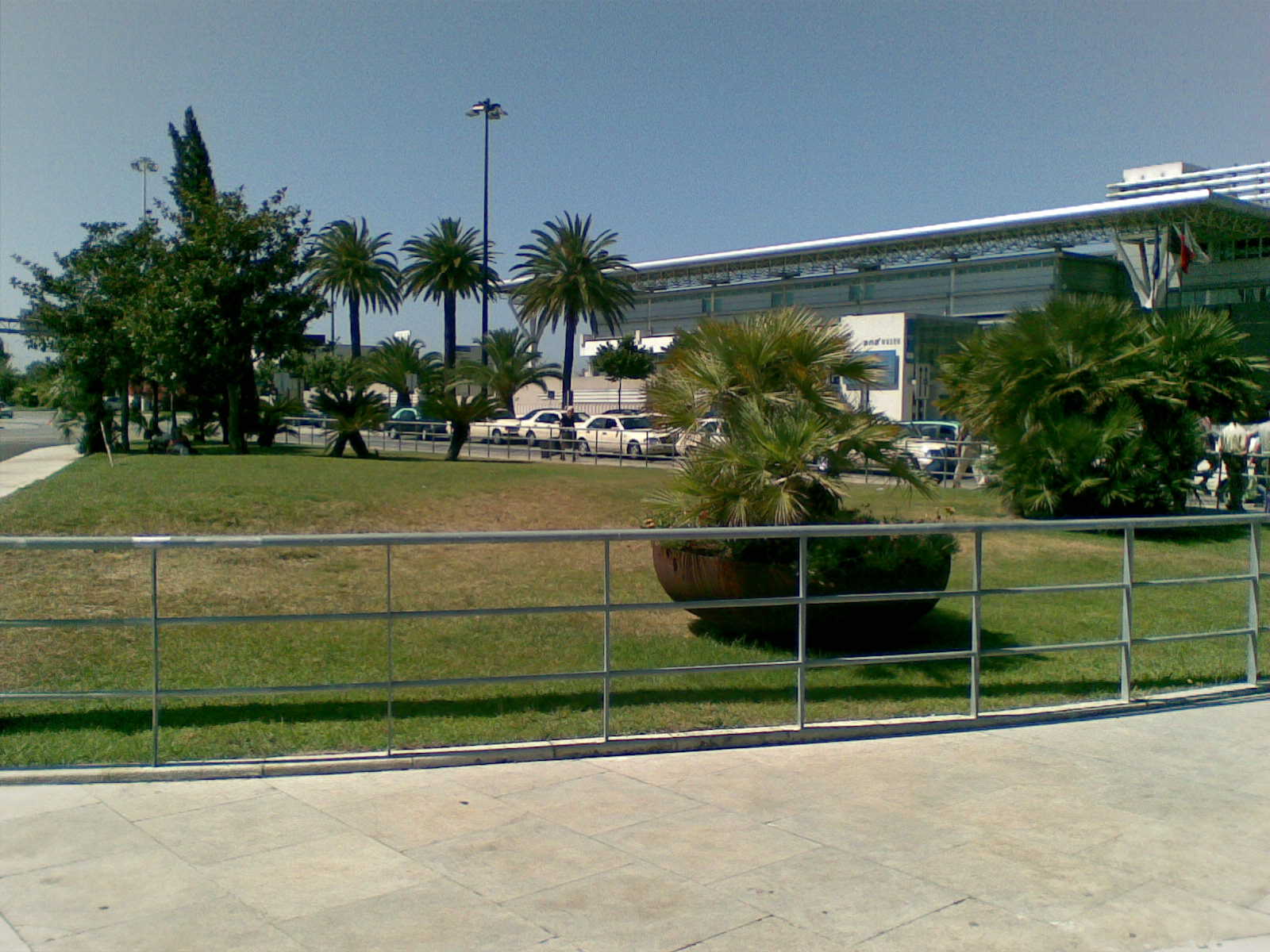 a gate in the middle of a park area that features a tree, fence, and a building