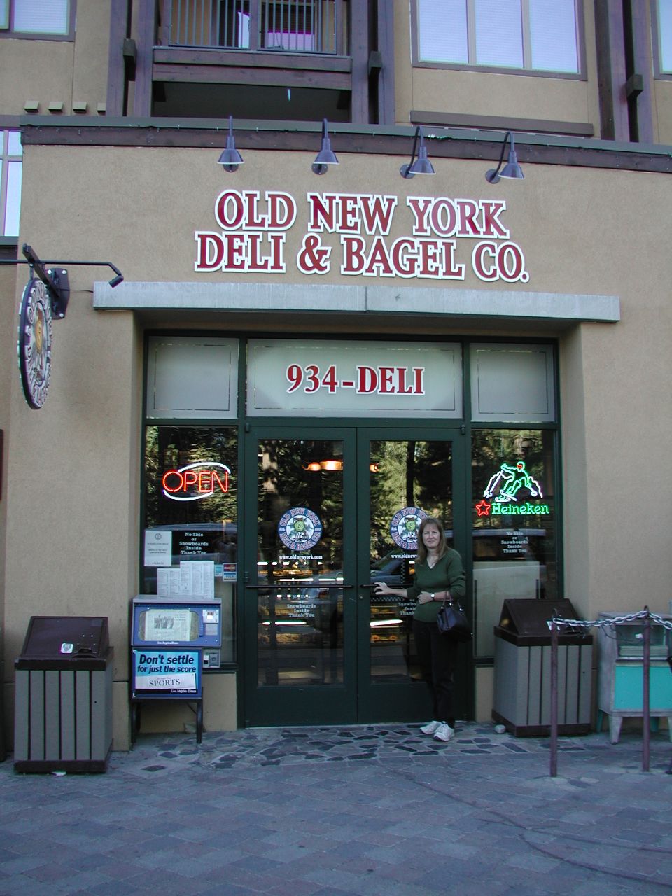 a woman stands outside of a deli and bagel co