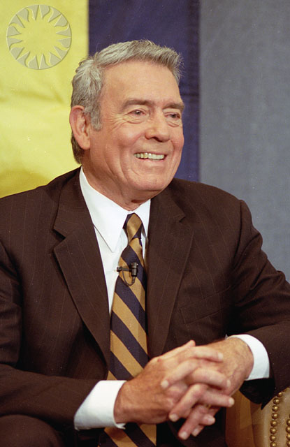 an older man in a suit and tie sits at a table smiling for the camera