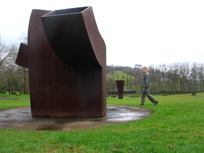 a person walks past a large sculpture in the middle of a park