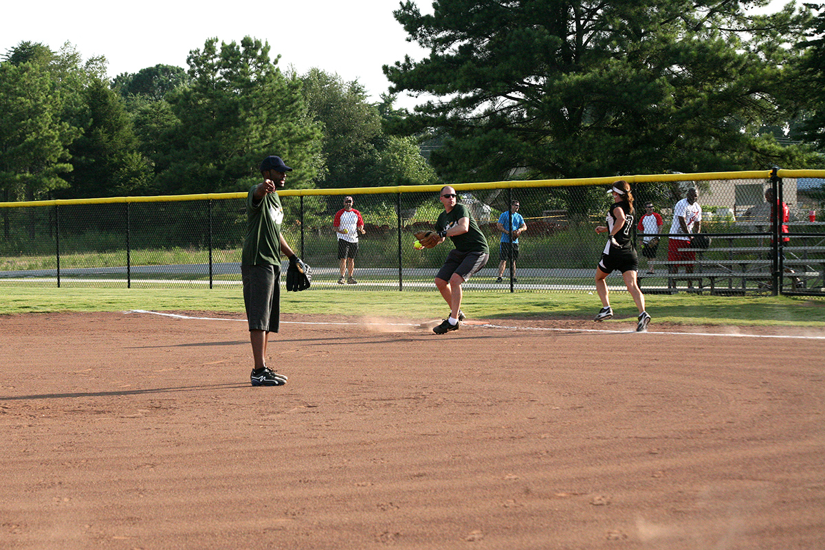 several softball players on the baseball field with the ball about to be pitched