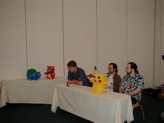 three men sitting at a table with nintendo wii game controllers