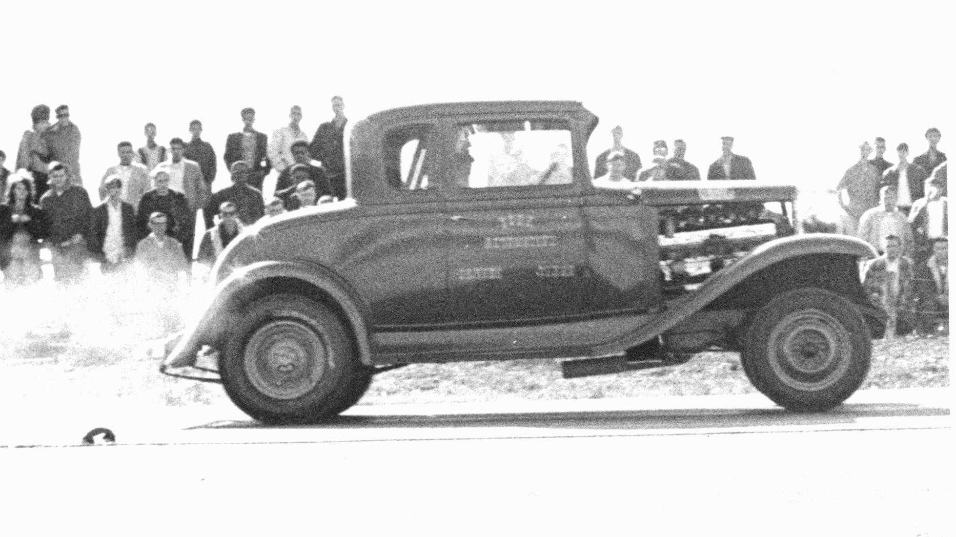 an old pick - up truck in front of a large group