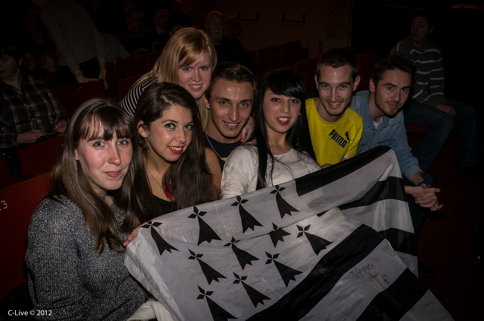 a group of people smiling while holding up a large flag