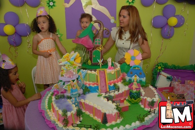 s standing around a birthday cake with a doll on the table