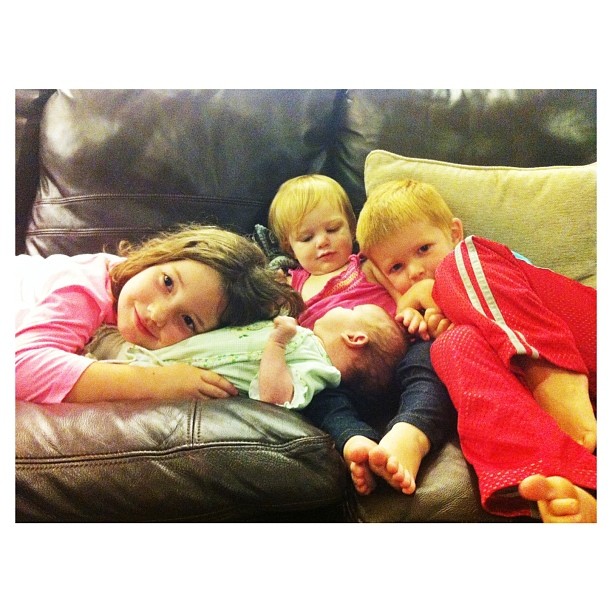 four children are laying together on a couch