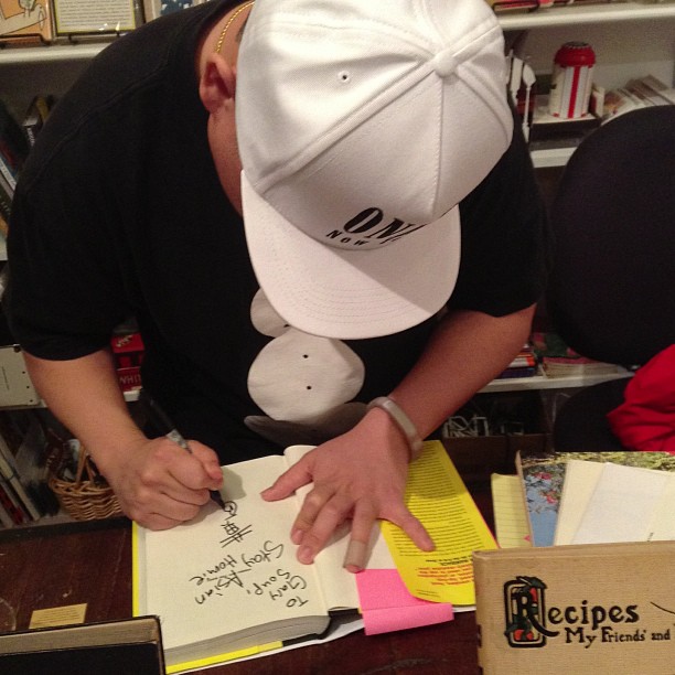 a man in black shirt and white hat bending over books