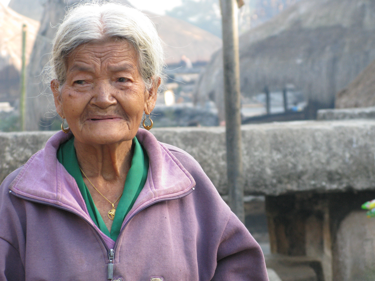 an old woman wearing a purple coat and a necklace