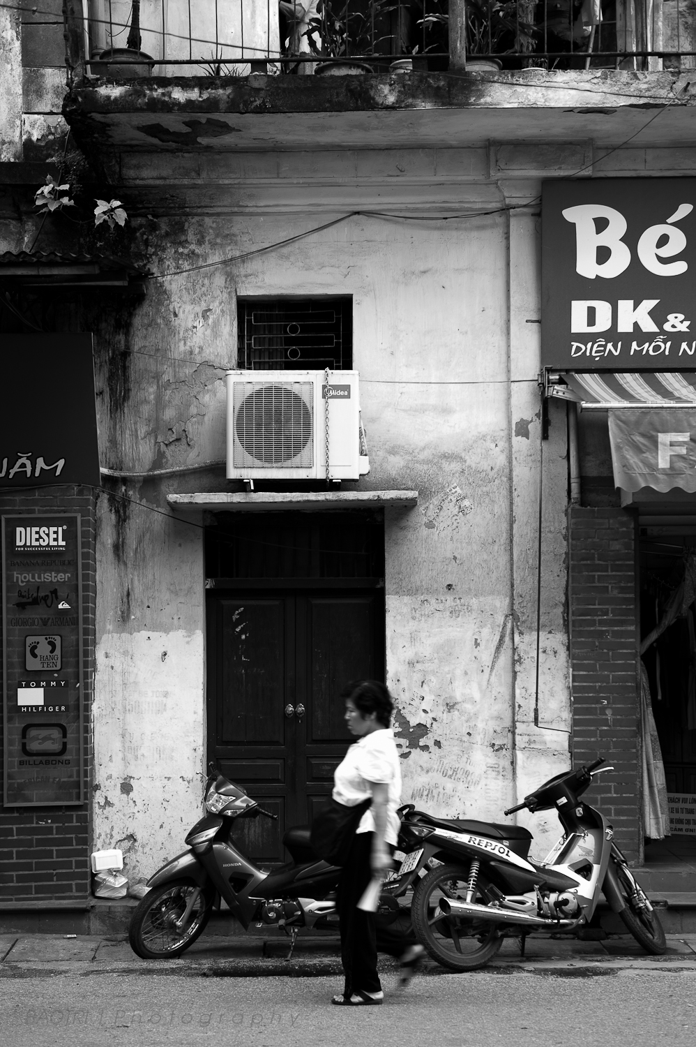 black and white pograph of man walking on the street in front of a parked motorcycle