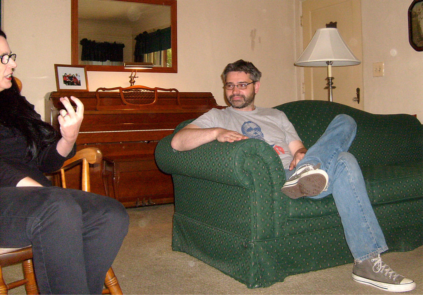 the man sits on the green chair with a woman looking on