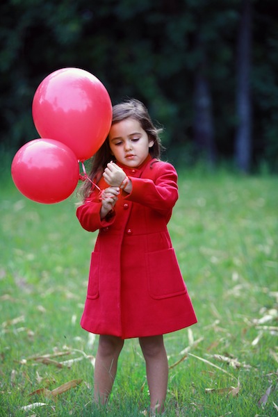 the  in a red coat is holding several balloons