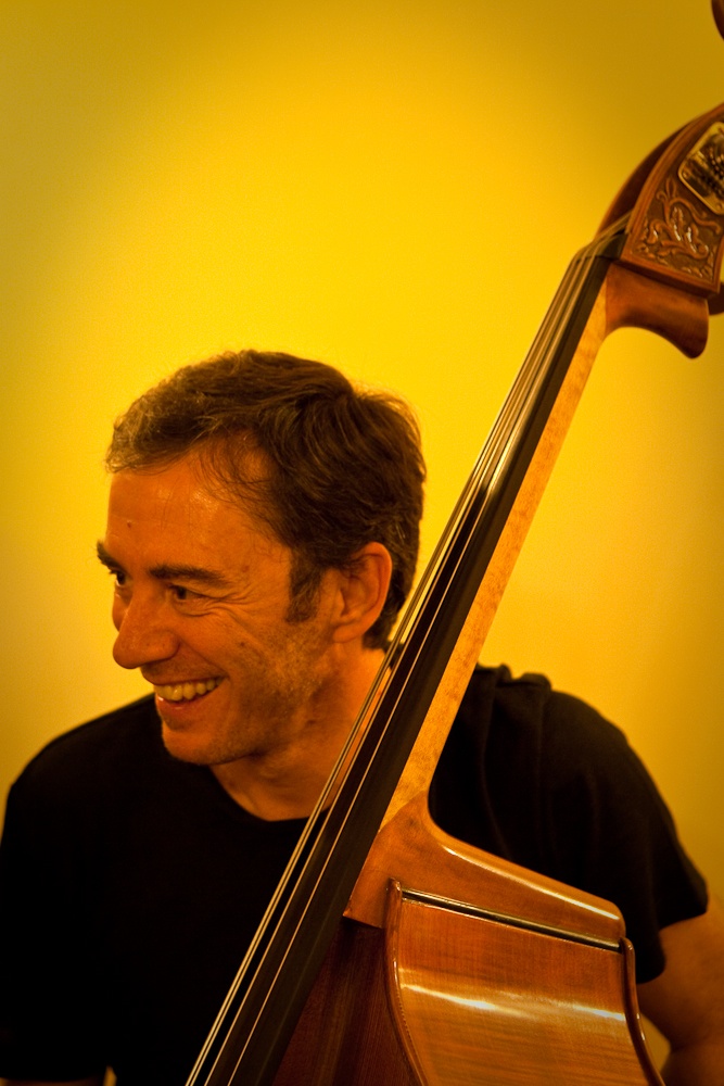 a smiling man holding a violin leaning on a wall