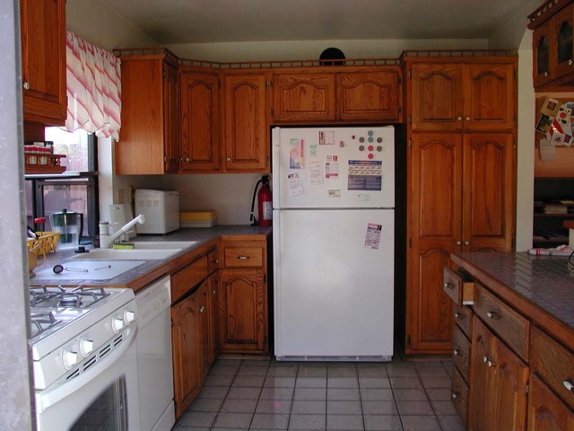 the kitchen features wood cabinets, tiled floor and white appliances