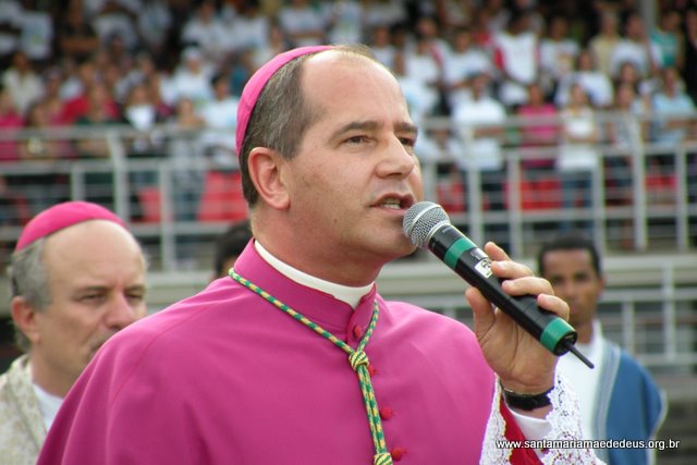 priest in large robe holding microphone in front of man