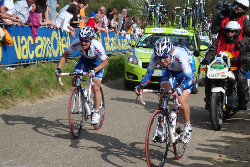 two cyclists race on the road and spectators watch