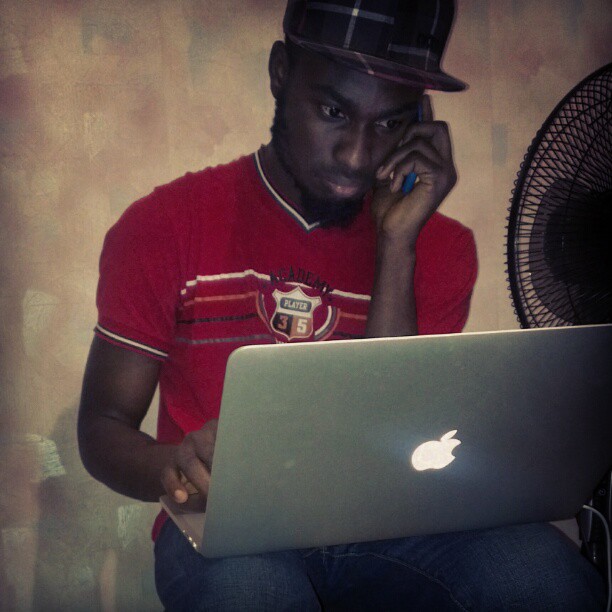 a man on a laptop sitting down with a hat on