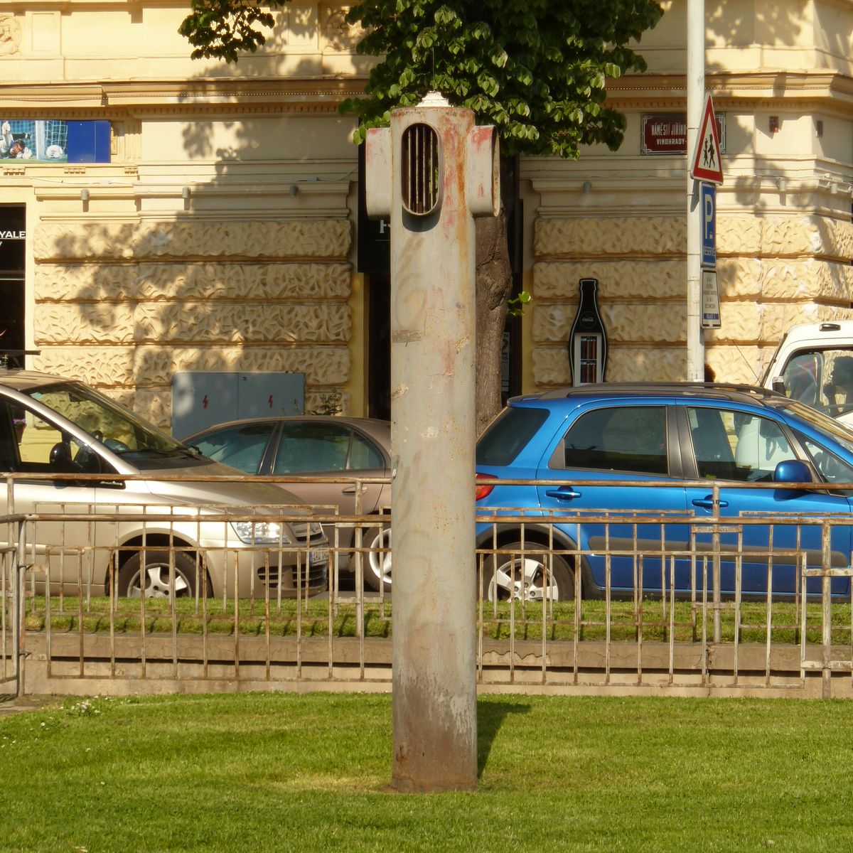 an old, rusted pole sits in the grass next to a blue car