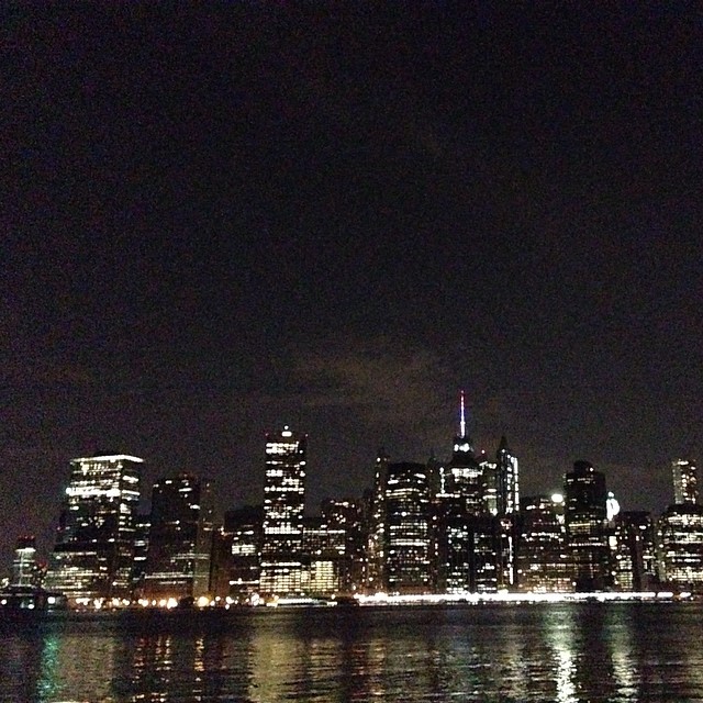 a night view of the new york skyline with reflection in the water