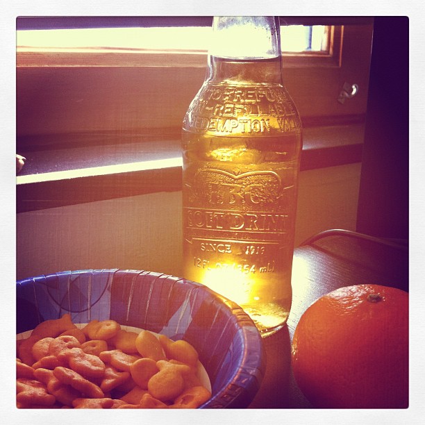 a bowl of cereal and an orange on the counter next to a drink bottle