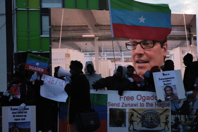 a man standing in front of a sign with a flag and a banner with the image of john fogden
