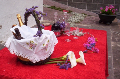 flowers and a wine bottle on a red mat next to a basket of wine and wine glasses