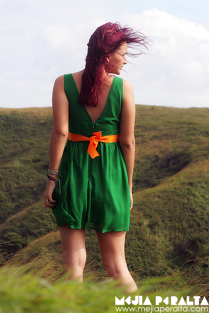 a girl with red hair wearing green clothing on a hill top