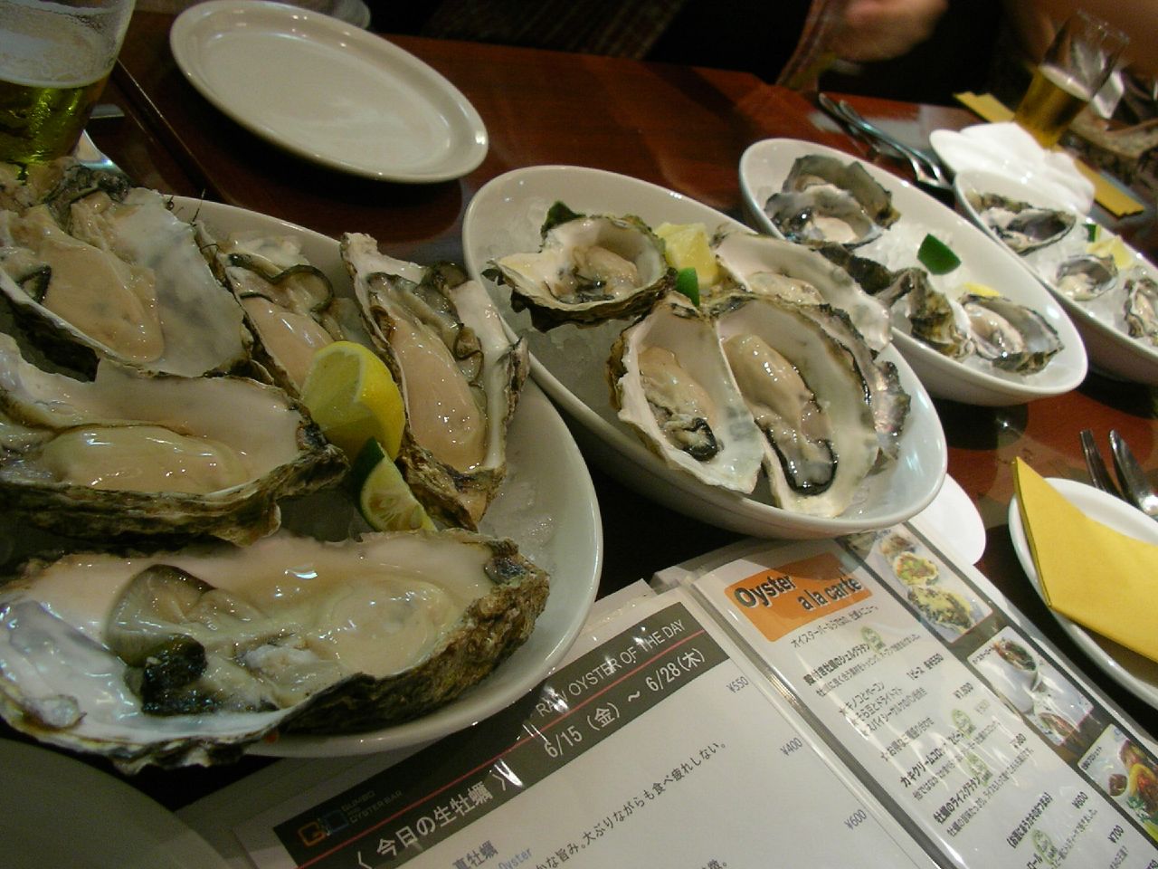 many plates filled with large raw oysters and some lemon slices on a table